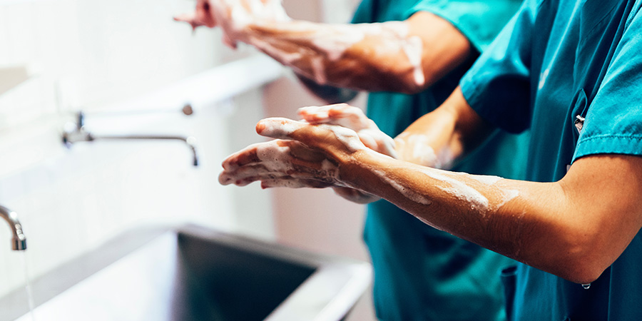 two people wearing teal colored scrubs standing at a sink washing their hands