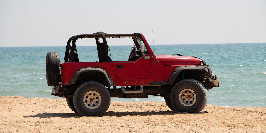 red jeep without top sitting on sand near water