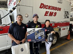 two men and one woman standing in front of Dickinson EMS ambulance