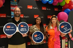 UTMB employees Ben Shapley, Iesha Johnson and Clarissa Ortiz hold silly signs in front of UTMB backdrop during May 2 lecture series event in Clear Lake