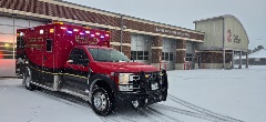 image of a red and black ambulance in snow in front of a fire station. text in image says "League City Fire Department." A large no. 2 is on the building