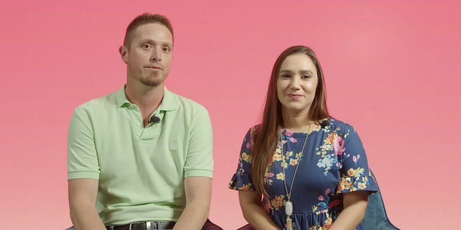 image of caucasian male wearing a light green polo sitting next to a caucasian female wearing a navy dress with a floral pattern. they have a pink background behind them
