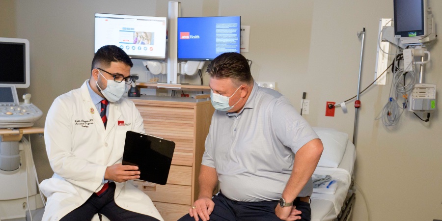 caucasian physician with white coat and surgical mask holding a clip board pointing to something with a male patient