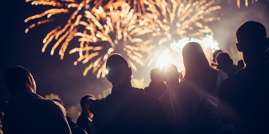 Silhouetted crowd watches bright fireworks exploding in a night sky during an outdoor celebration, illustrating Fourth of July festivities and fireworks displays