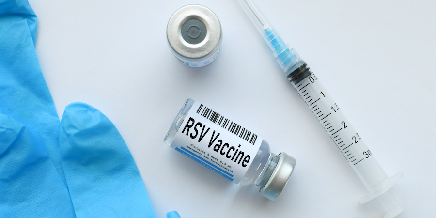 RSV vaccine vial labeled “RSV Vaccine” next to a syringe, protective gloves, and a small medicine vial on a clean white surface, representing immunization and respiratory virus protection