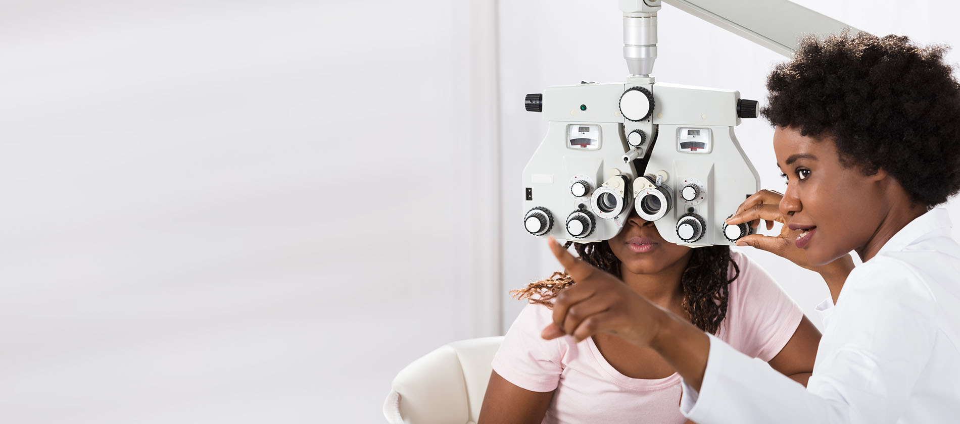 An optometrist guides a patient through a vision test using a phoropter during a routine eye exam.