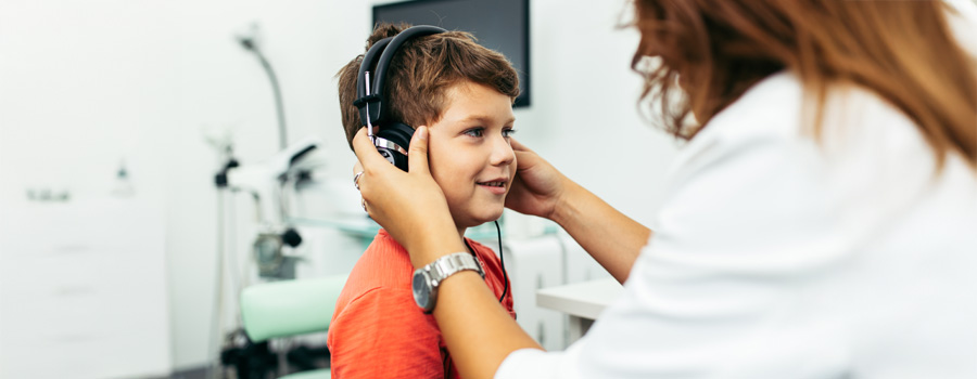A young boy wears headphones during a hearing test conducted by a pediatric audiologist.