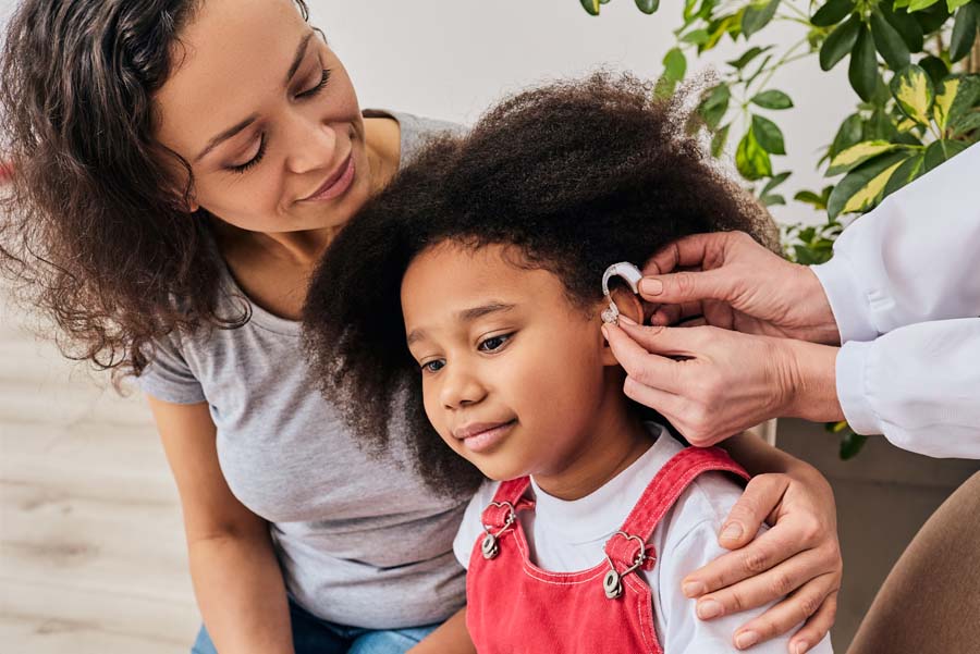 Child with her mother trying on a hearing aid by audiologist at a hearing clinic