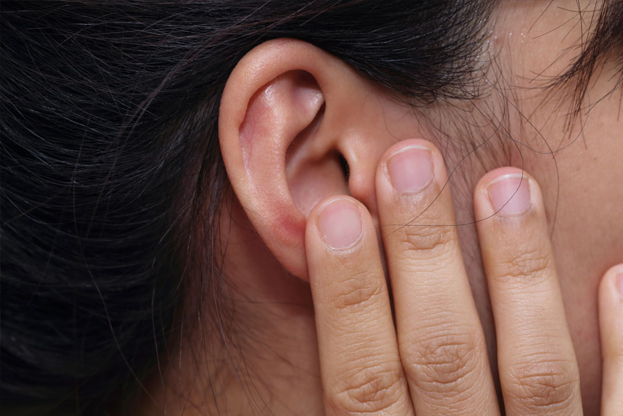 A woman touches her ear with her hand, showing discomfort or ear pain.
