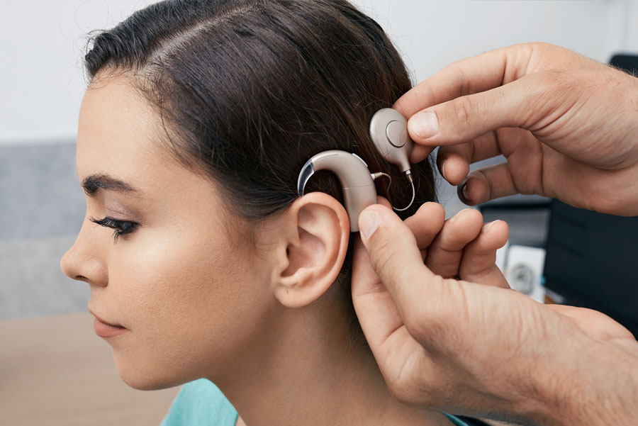 A close-up of a health professional fitting a cochlear implant device on a woman’s ear.