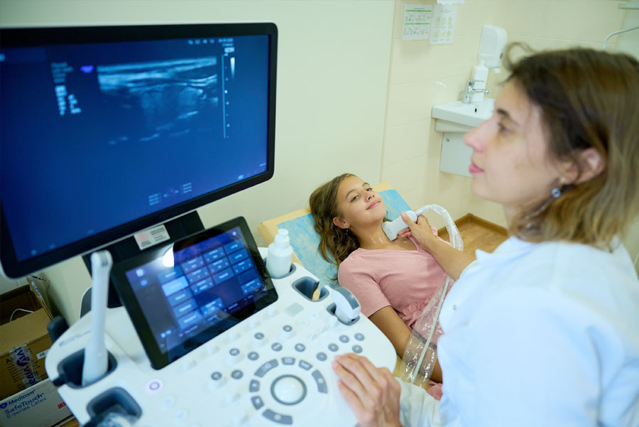 Female doctor making thyroid sonogram for female child patient