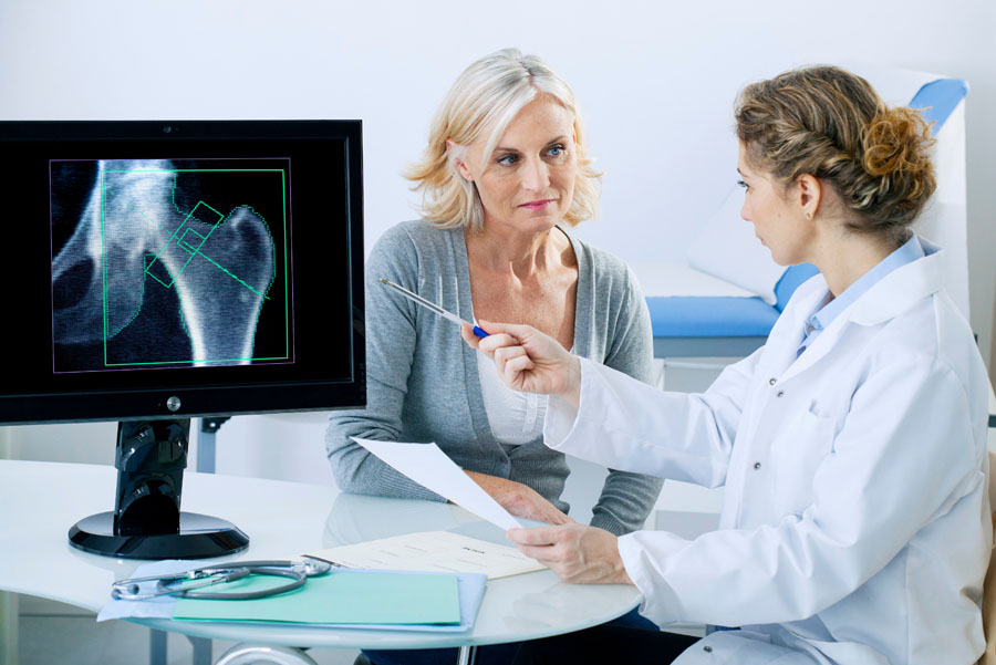 Female doctor showing female patient X-ray on screen of hip