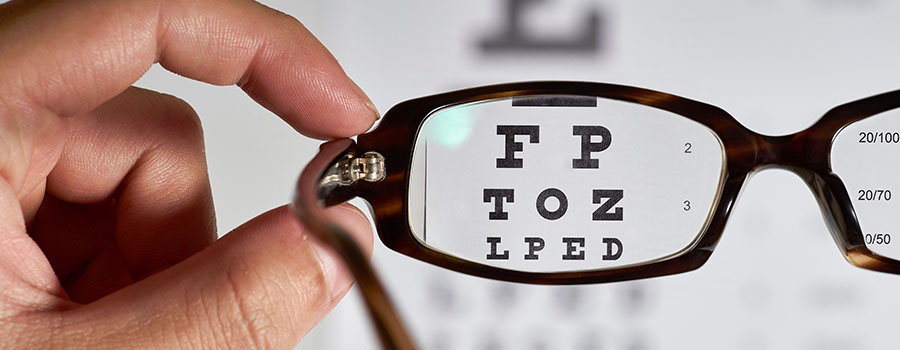 A person holds up glasses in front of an eye chart, clearly showing the test letters through the lens. 