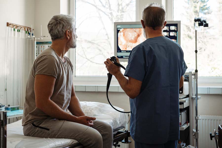 Male doctor explaining colonoscopy results to male patient using monitor images