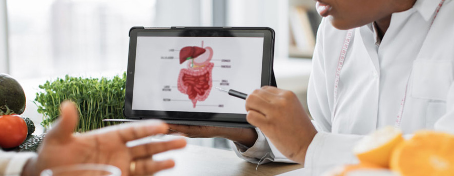 Nutrition specialist in doctor's coat showing digital device with photo of digestive system to patient