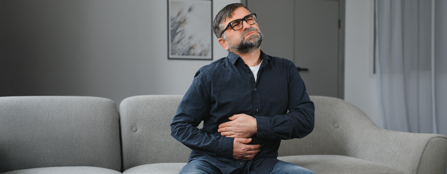 Man seated on living room sofa in pain, touching his stomach