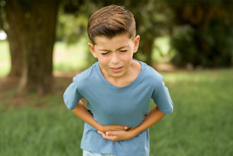 Young boy with eyes closed standing outside with hands on his stomach while experiencing stomach pain