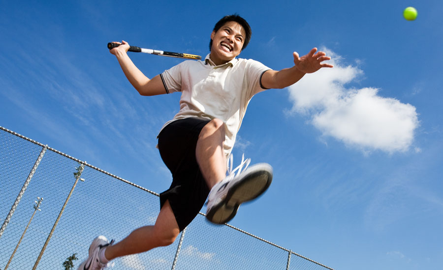 Man jumping in the air, playing tennis outdoors