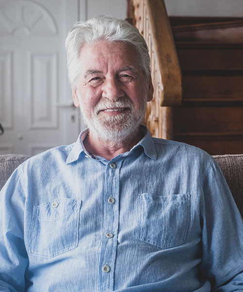 A man in his 70s smiling and sitting on a couch in his living room