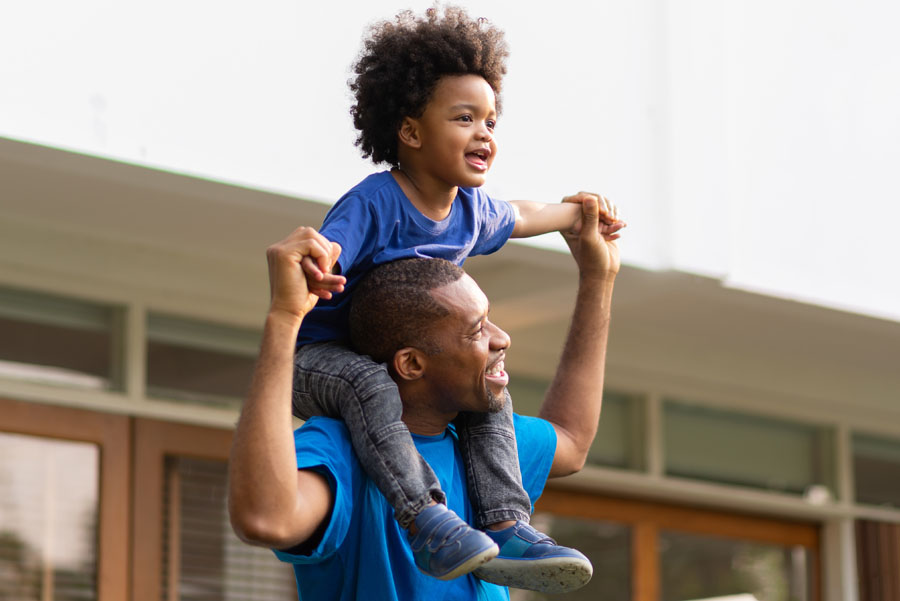 Happy man with smiling young child sitting on his shoulders outdoors
