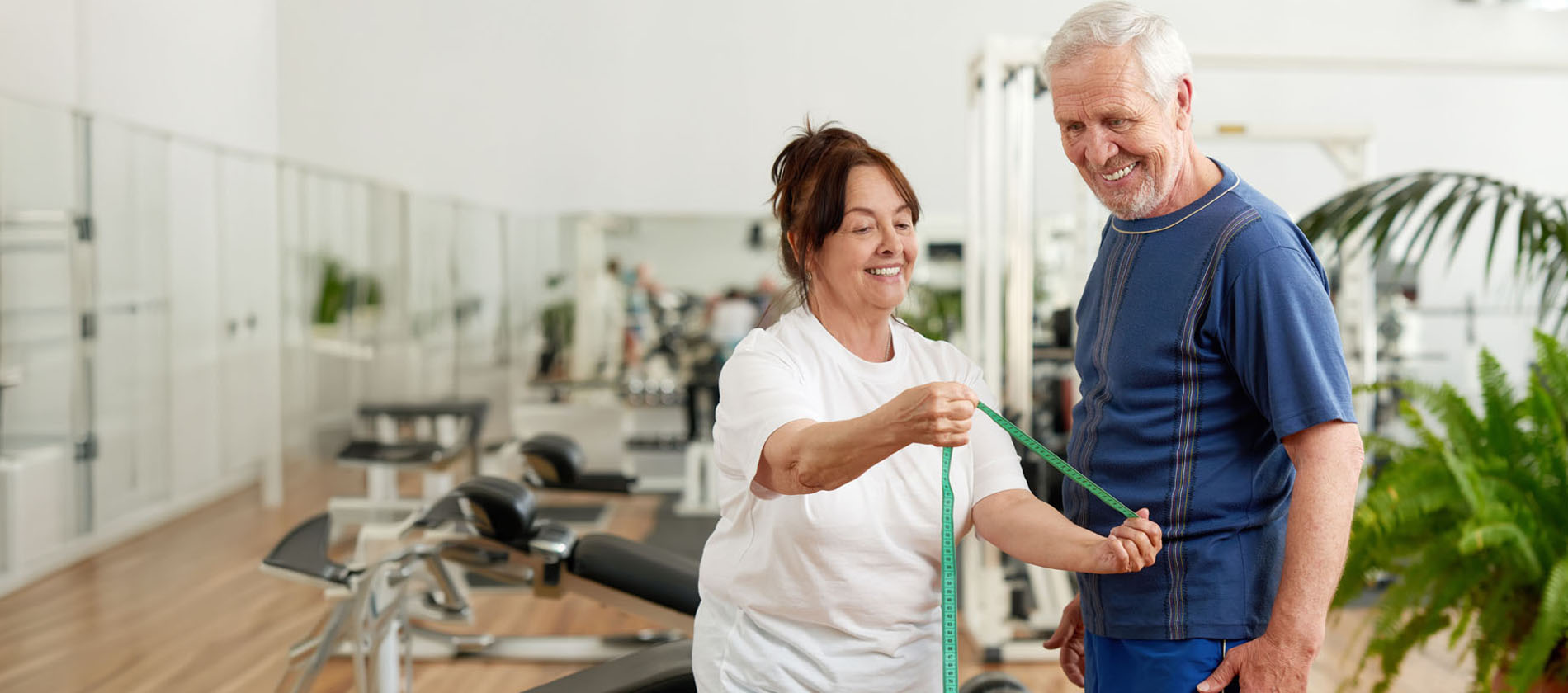 Woman showing elderly man a measuring tape at fitness club to show her weight loss progress