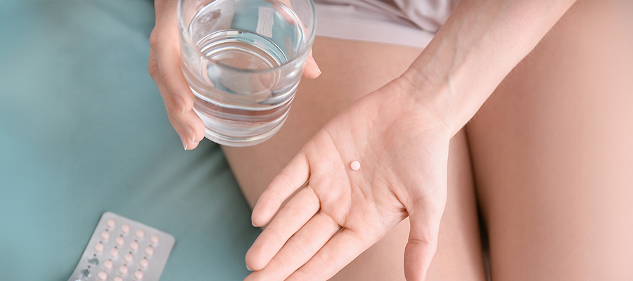 A person holds a pill and glass of water, showing hormone or birth control treatment.