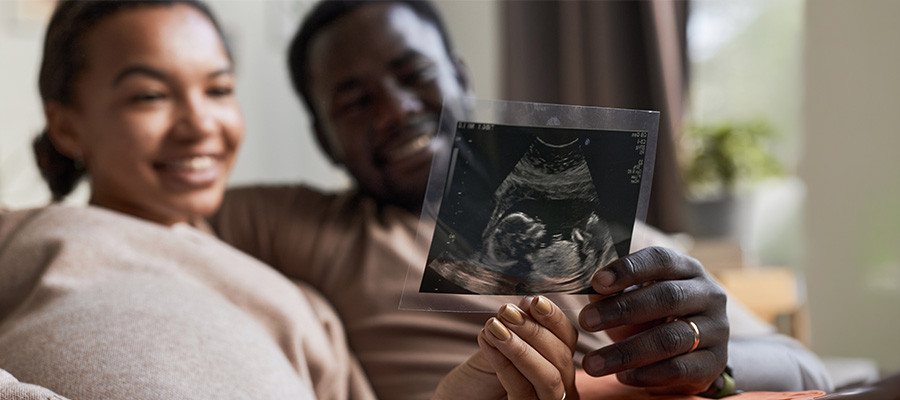 A pregnant couple smiles while holding an ultrasound image during prenatal care with UTMB Health maternal-fetal medicine.