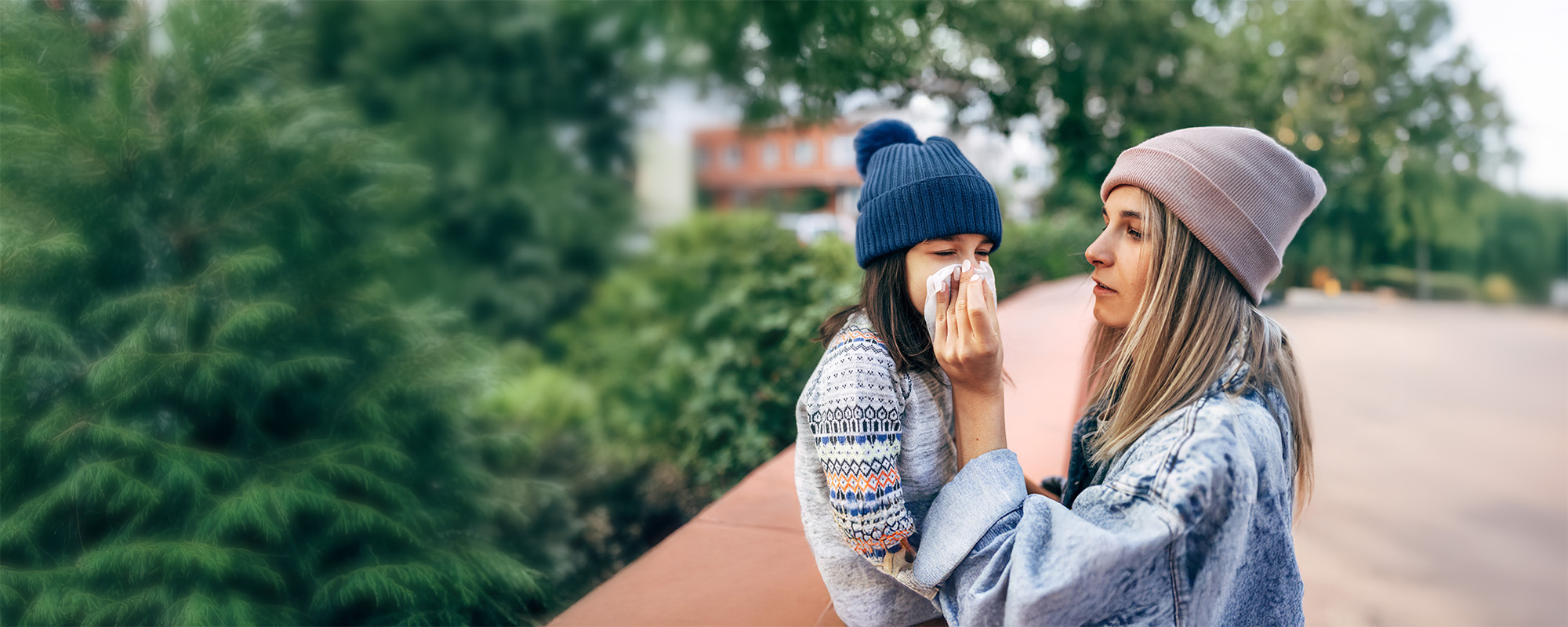A mom wiping her child's nose in an outdoor setting