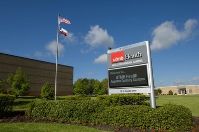 Exterior view of UTMB Health’s Angleton Danbury Campus, showing the campus sign in front of the hospital building with landscaped grounds, an American flag, and clear blue sky