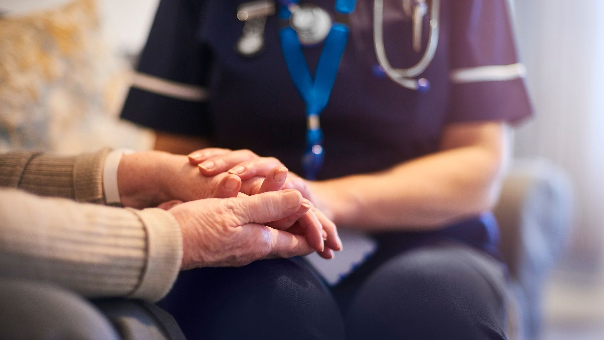 A health care provider holds an older patient's hands