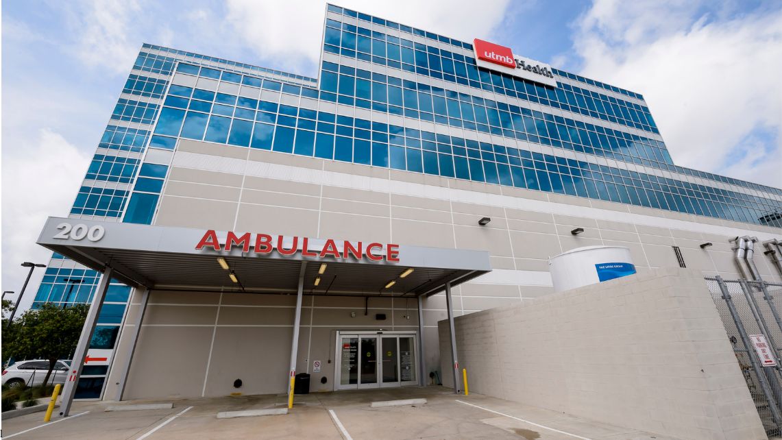 Exterior view of the UTMB Health Clear Lake Campus showing the multistory hospital building with glass windows and the covered ambulance entrance marked “AMBULANCE,” reflecting its designation as a Level II Trauma Center