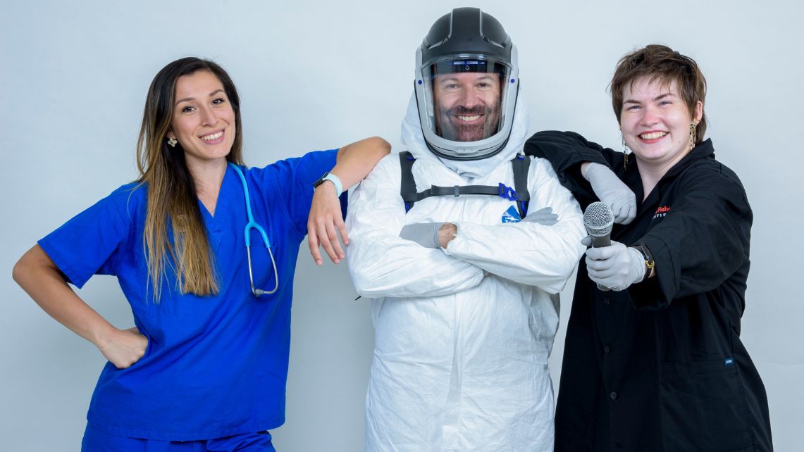 A picture of Dr. Dennis Bente in a space suit with Infectious Science Podcast cohost Christina Rios and Camille Ledoux  standing next to him