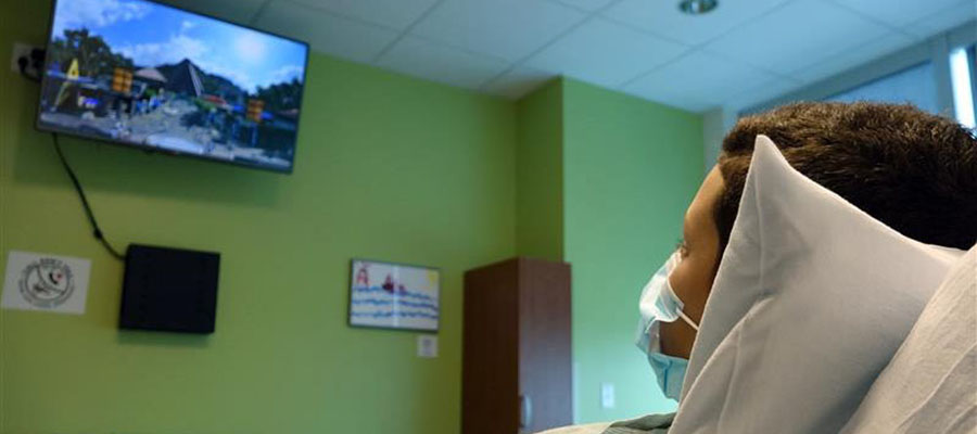 A child in a hospital bed stares at a TV screen.