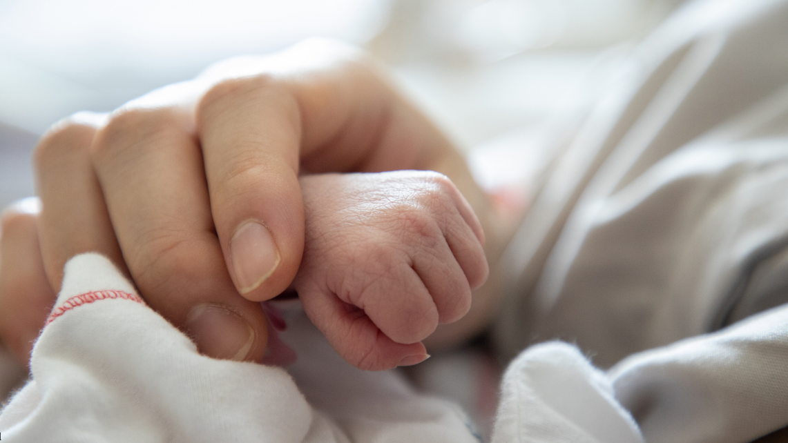 A mother holds the tiny hand of a preterm baby
