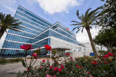 Exterior view of the UTMB Health Clear Lake Campus building with palm trees and landscaped flowers in the foreground.