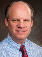  Man in this professional head-and-shoulder image is bald on top and is wearing a light blue shirt with a brown tie. 