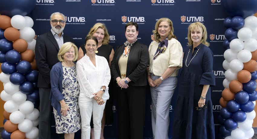 Seven people stand in two rows in front of a UTMB‑branded backdrop, flanked by balloon columns in navy, white, and orange.