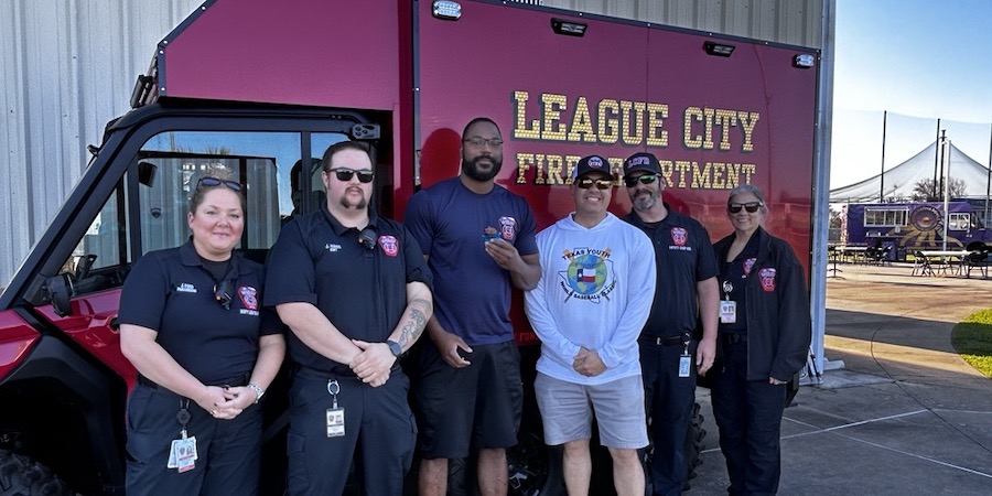 image of Firefighters standing in uniform in front of one of their vehicles. they are smiling and a representative from UTMB Health  is pictured with them in white shirt and ball cap