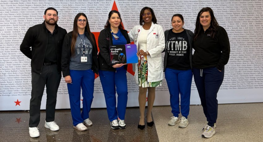 Six people stand in a row in front of a backdrop covered in dense text and red stars, with one person in the center holding a certificate folder while wearing a white lab coat.